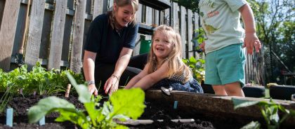 Gardening at Kindred Huntingdon A teacher and two children are happily planting seedlings in an outdoor raised garden bed at the nursery.