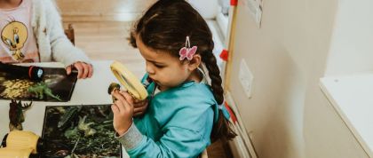Insect Hunting at Kindred Little Learners A girl uses a magnifying glass to inspect an insect