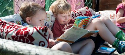 Outdoor canopied area for reading and relaxing at Kindred Huntingdon Two children reading and smiling on the sofa outside